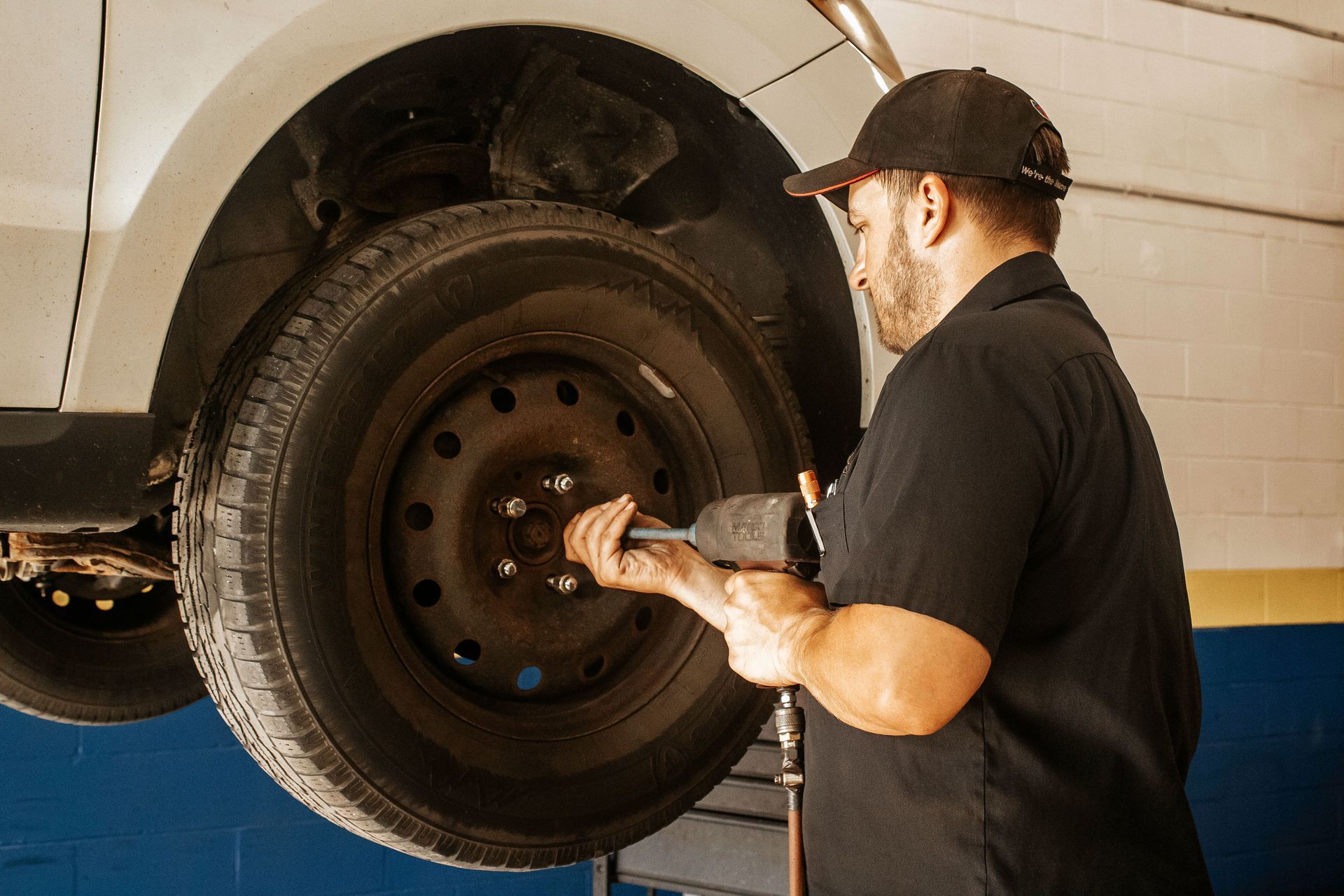 Mechanic using an impact wrench to remove a car tire in a garage.