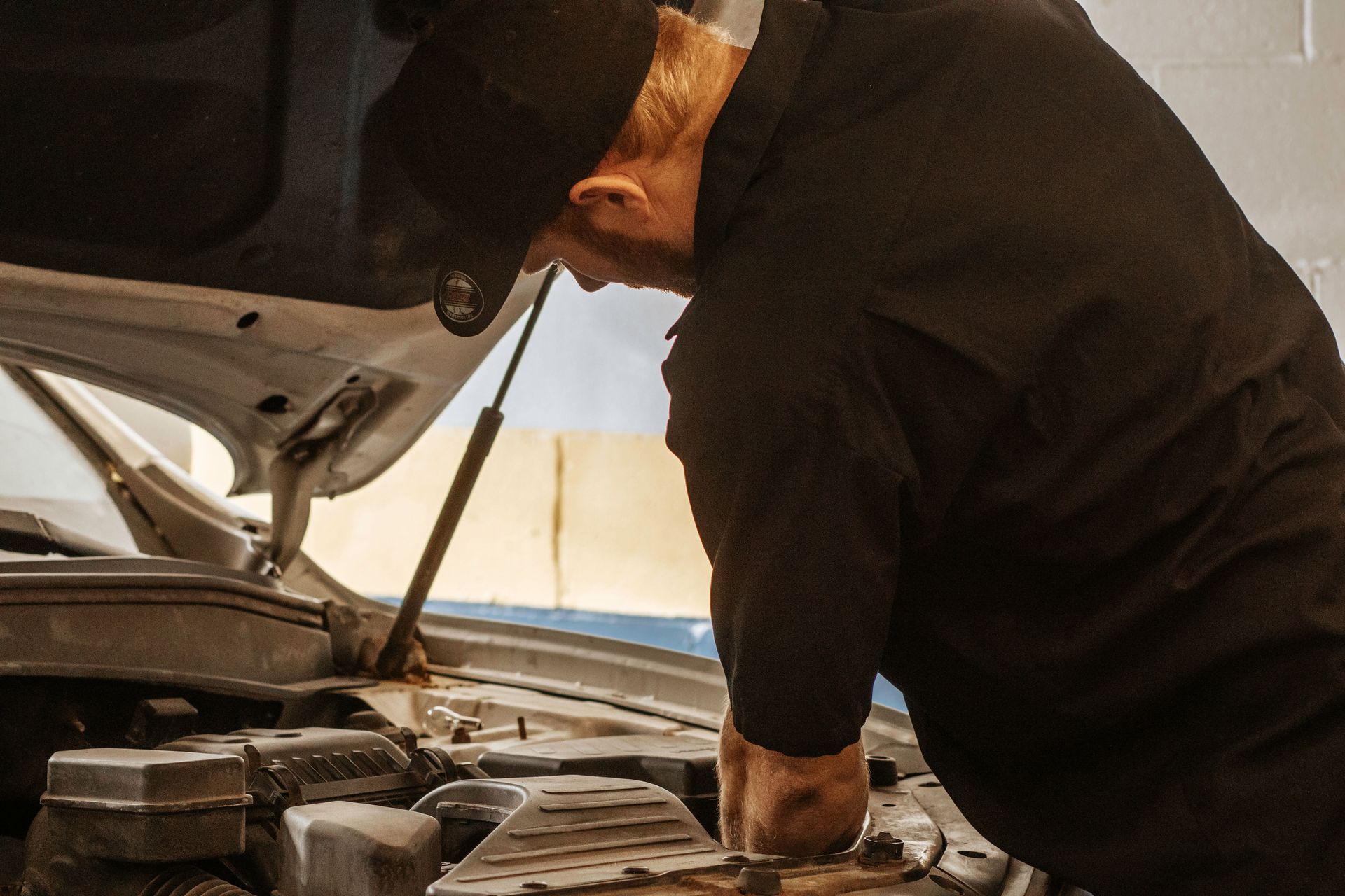 Mechanic in black uniform working on a car engine, in a garage.