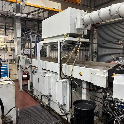 A large machine is sitting in a factory next to a black bucket.