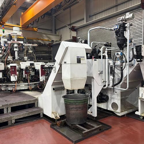 A large machine is sitting in a factory next to a bucket.