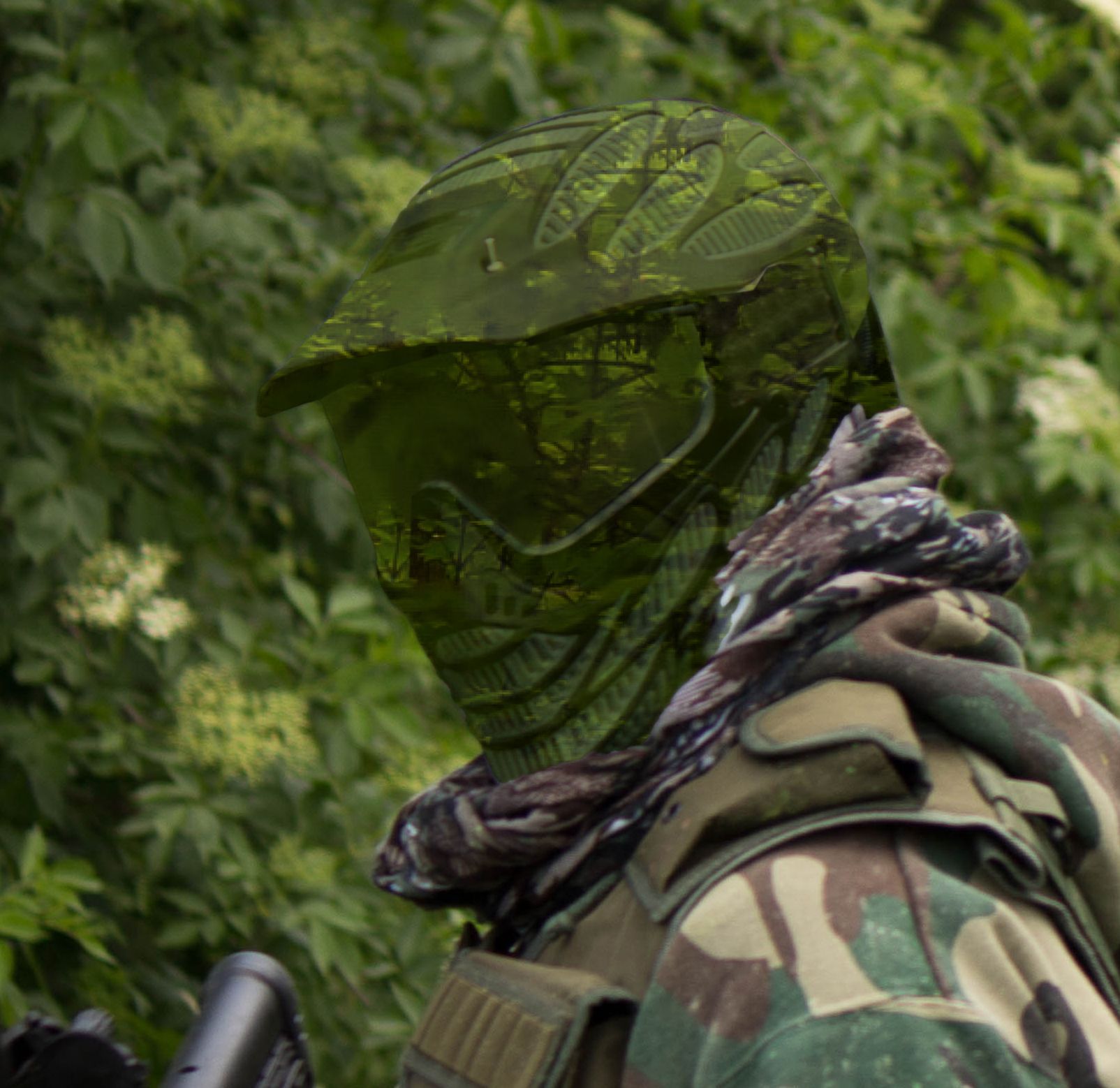 Airsoft player wearing helmet and goggles covered with GOShelter Weathercock Camo Film in with forest overlay, in a wooded area.