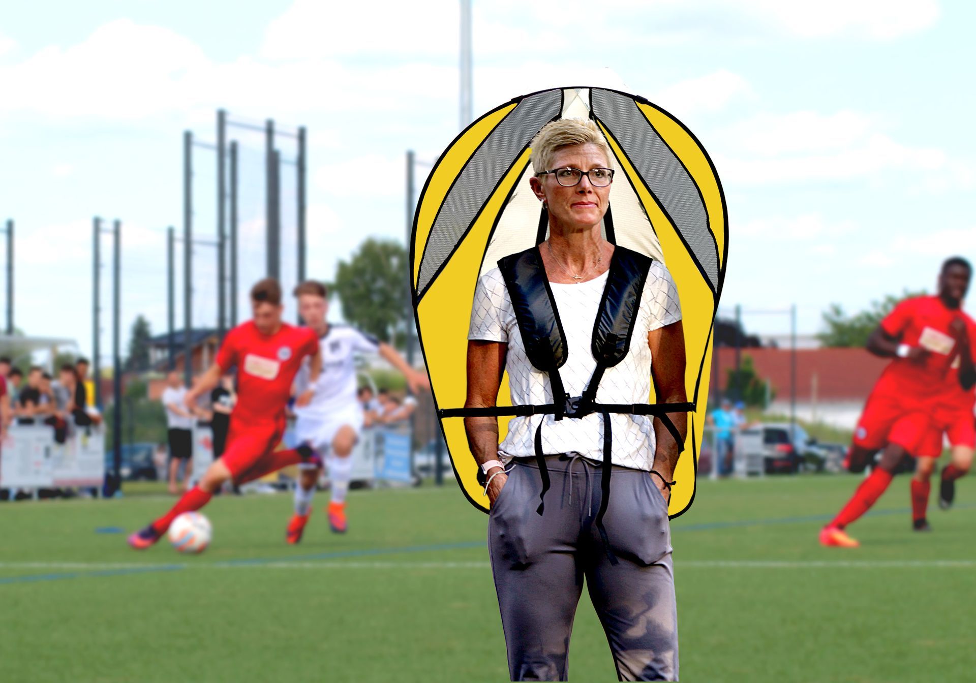 Woman wearing a GOShelter Shade sun/rain protective gear stands on a soccer field as players compete in the background.