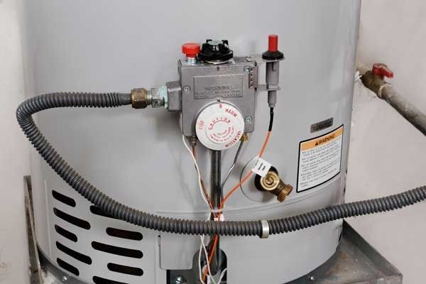 A gas water heater with a control panel, gas line, and pilot light in a utility room.