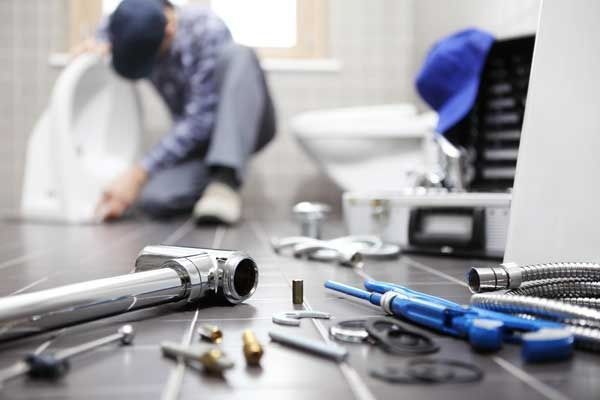 Plumber installing toilet in bathroom, tools scattered on the floor.