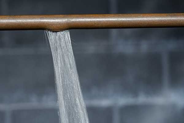 Copper pipe leaking water; grey block wall background.