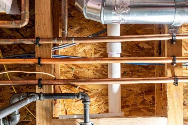 Pipes and ductwork installed in a wooden structure. Copper pipes secured with black clips; white drain pipe.