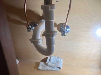 A white sink drain pipe, with a curve, under a bathroom sink with copper supply lines and a white valve.
