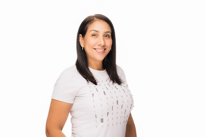 A woman in a white shirt is smiling and standing in front of a white background.