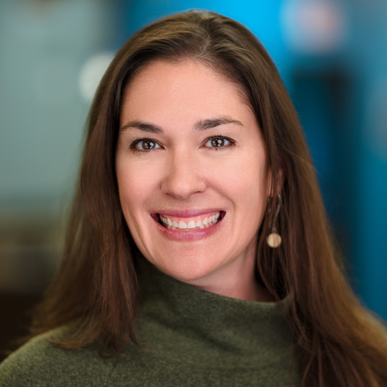 Woman with long brown hair smiles, wearing a green turtleneck.