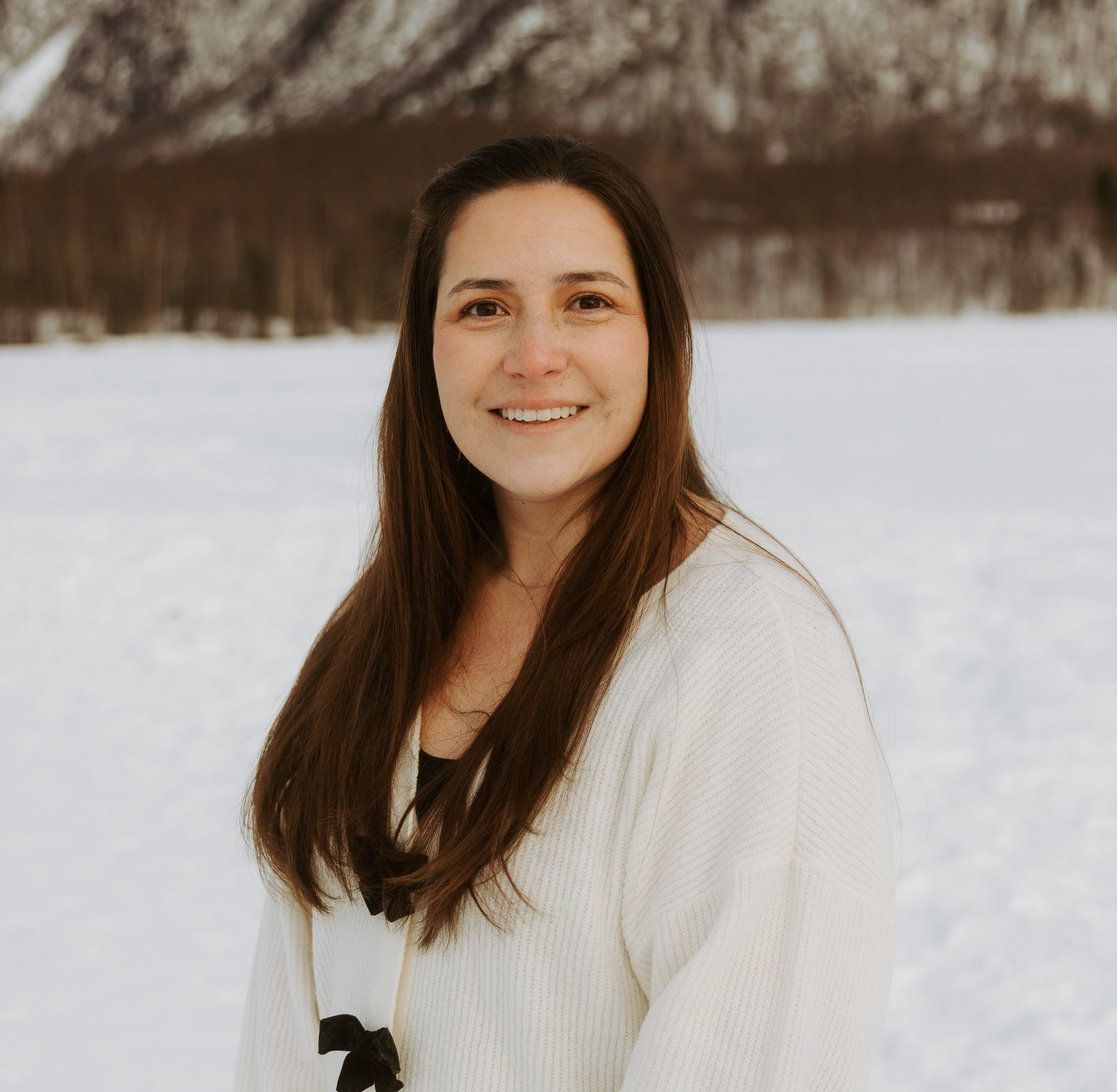 Woman with long dark hair, smiling. Wearing a white sweater with black bows.