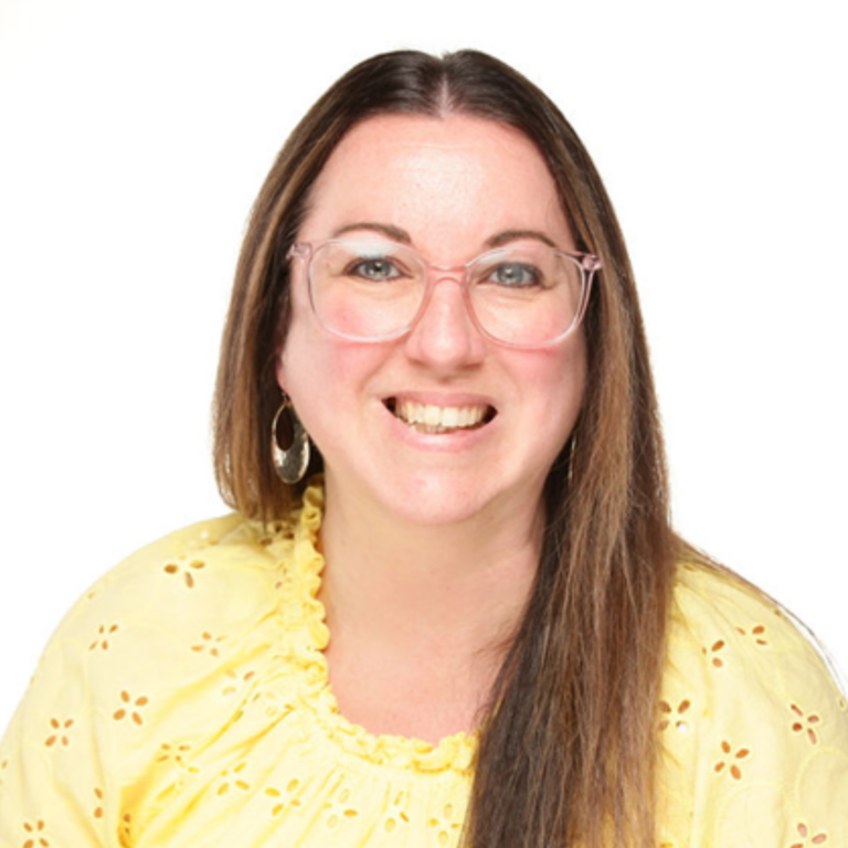 Woman with long brown hair, wearing glasses and yellow top, smiling.