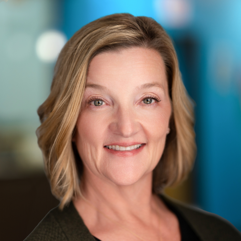 Woman with short blonde hair smiles in a professional headshot against a blurred blue background.