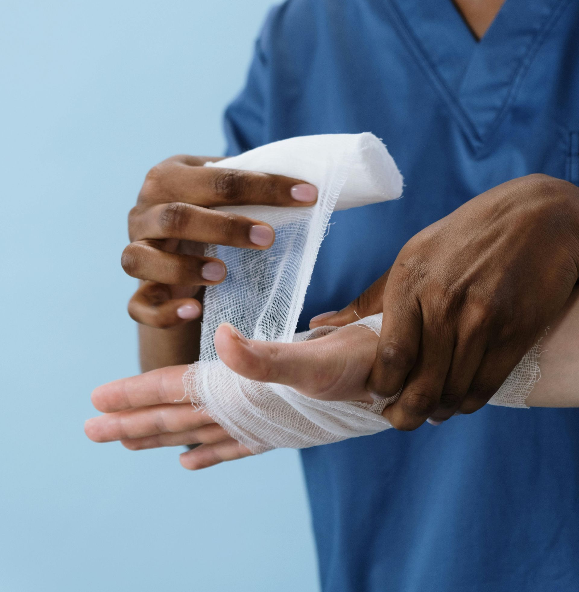 Hands wrapping a white bandage around another person's wrist against a light blue background.