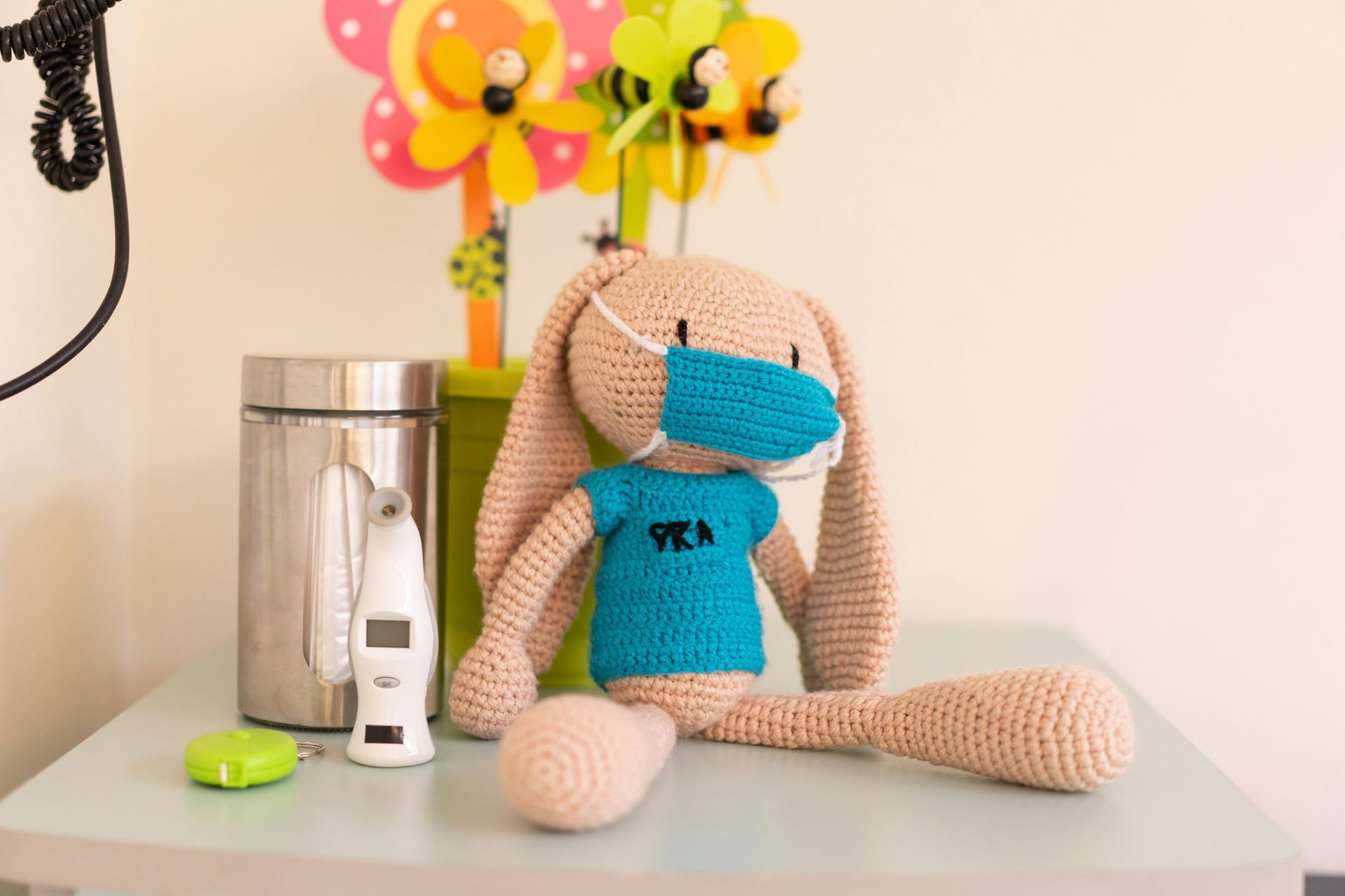 Crocheted bunny with face mask, thermometer, and decorative flowers on a table.