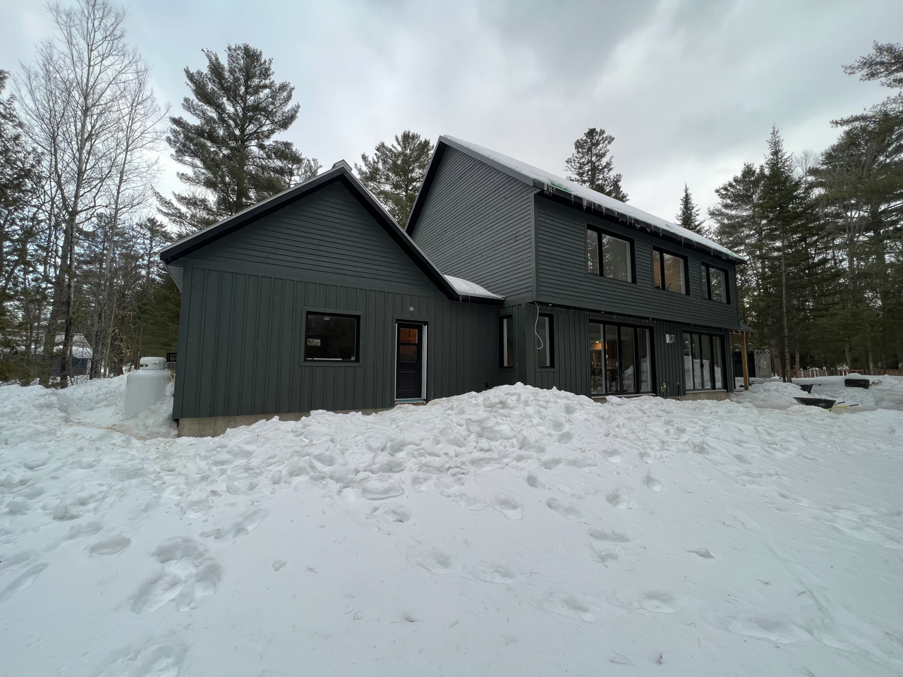 Une grande maison noire est entourée de neige et d'arbres.