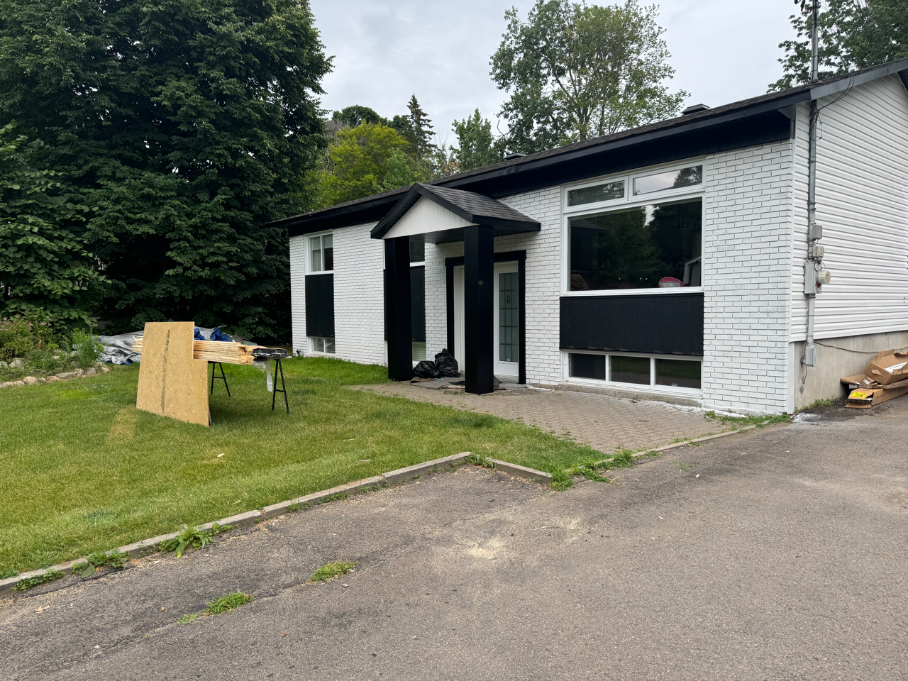 Une maison blanche avec des bordures noires est assise sur une pelouse verte luxuriante.