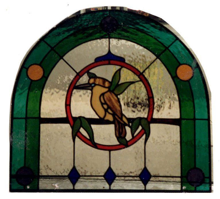 arch type leadlight window with green trim and a small bird on a branch
