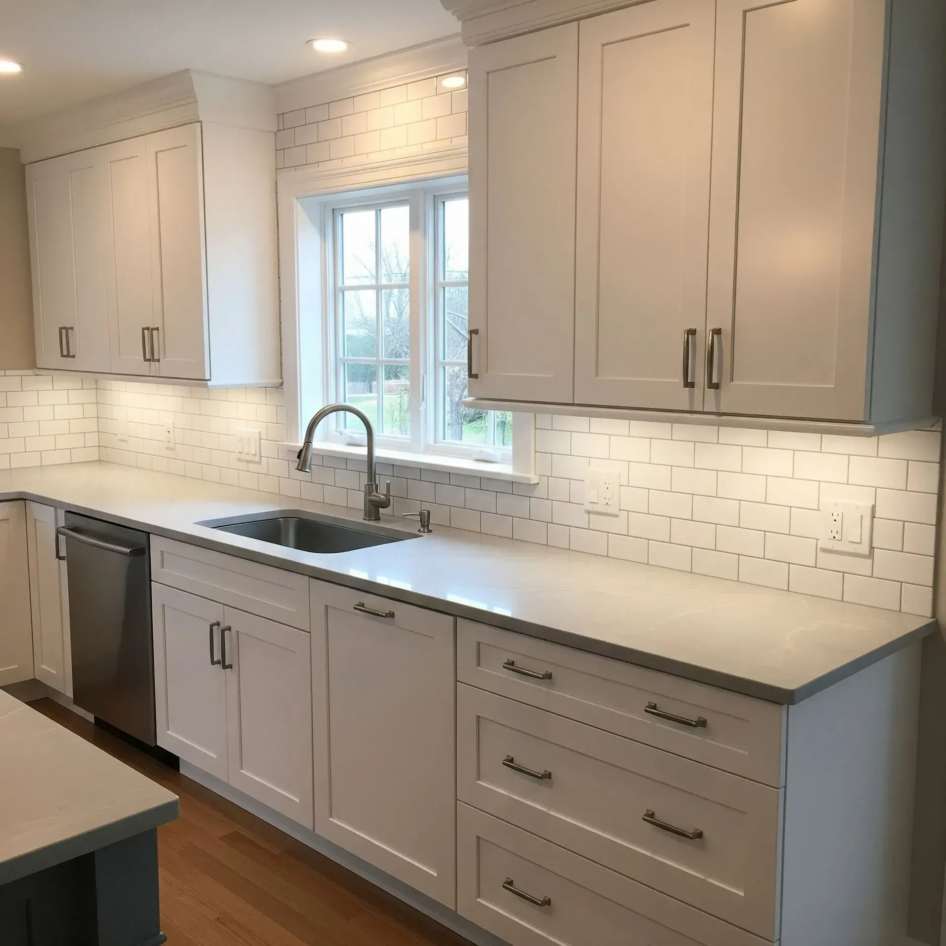 White kitchen cabinets with a gray countertop and a stainless steel sink.