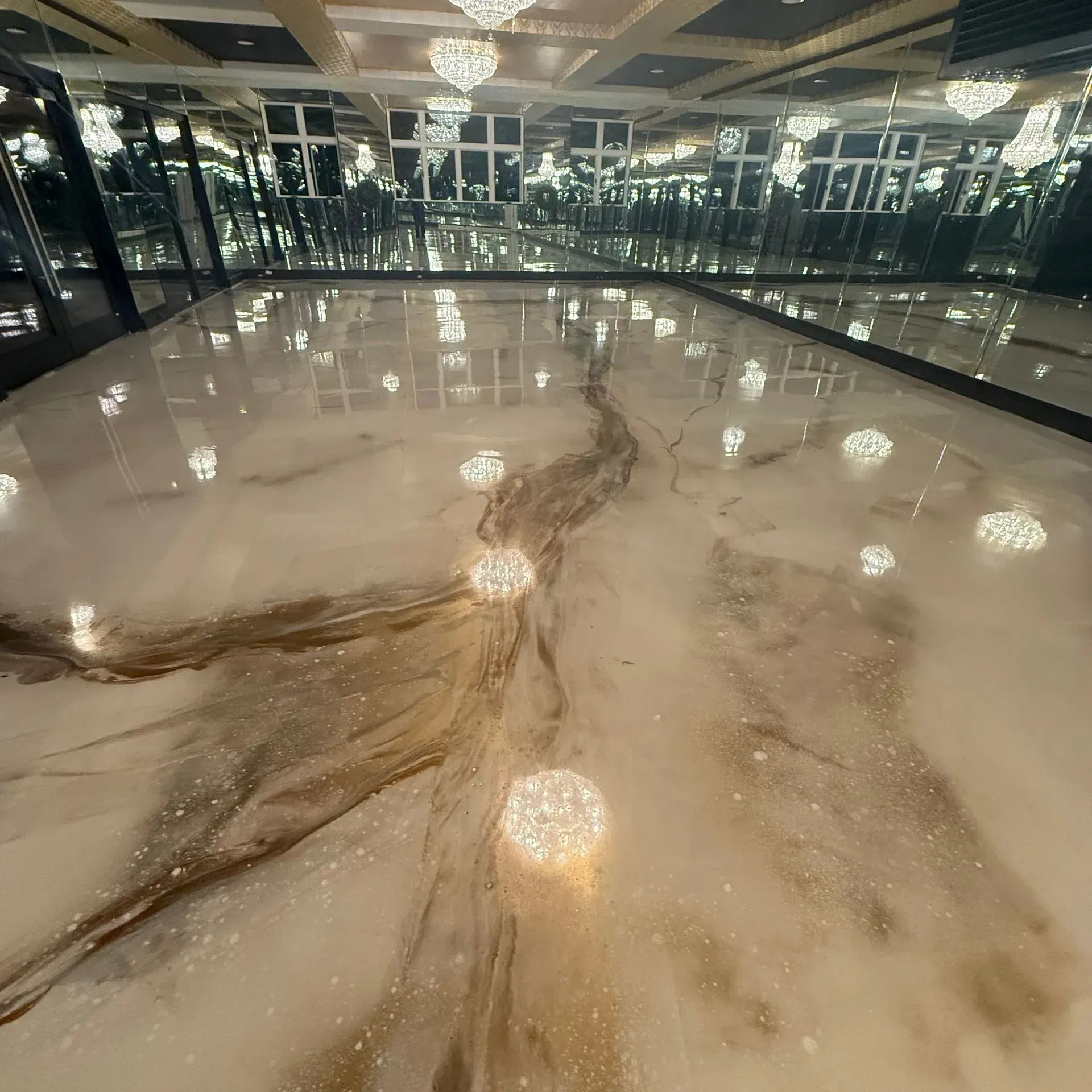Elegant room with a marble-like epoxy floor, gold veining, and mirrored walls; crystal chandeliers overhead.