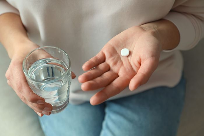 Woman holding abortion medications with a glass of water.