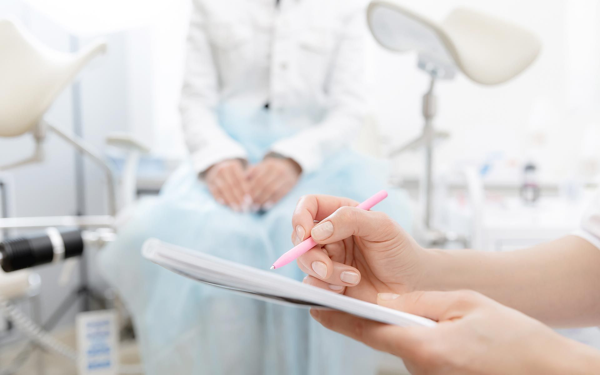 Person sitting in a medical exam room while a clinician writes notes on a clipboard.