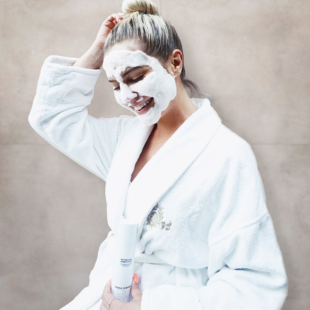 A woman in a white robe has a foam mask on her face