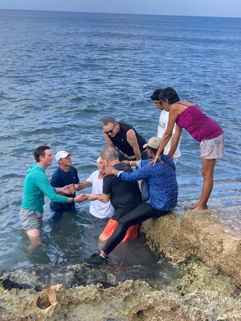 A group of people are standing on a rock in the ocean.