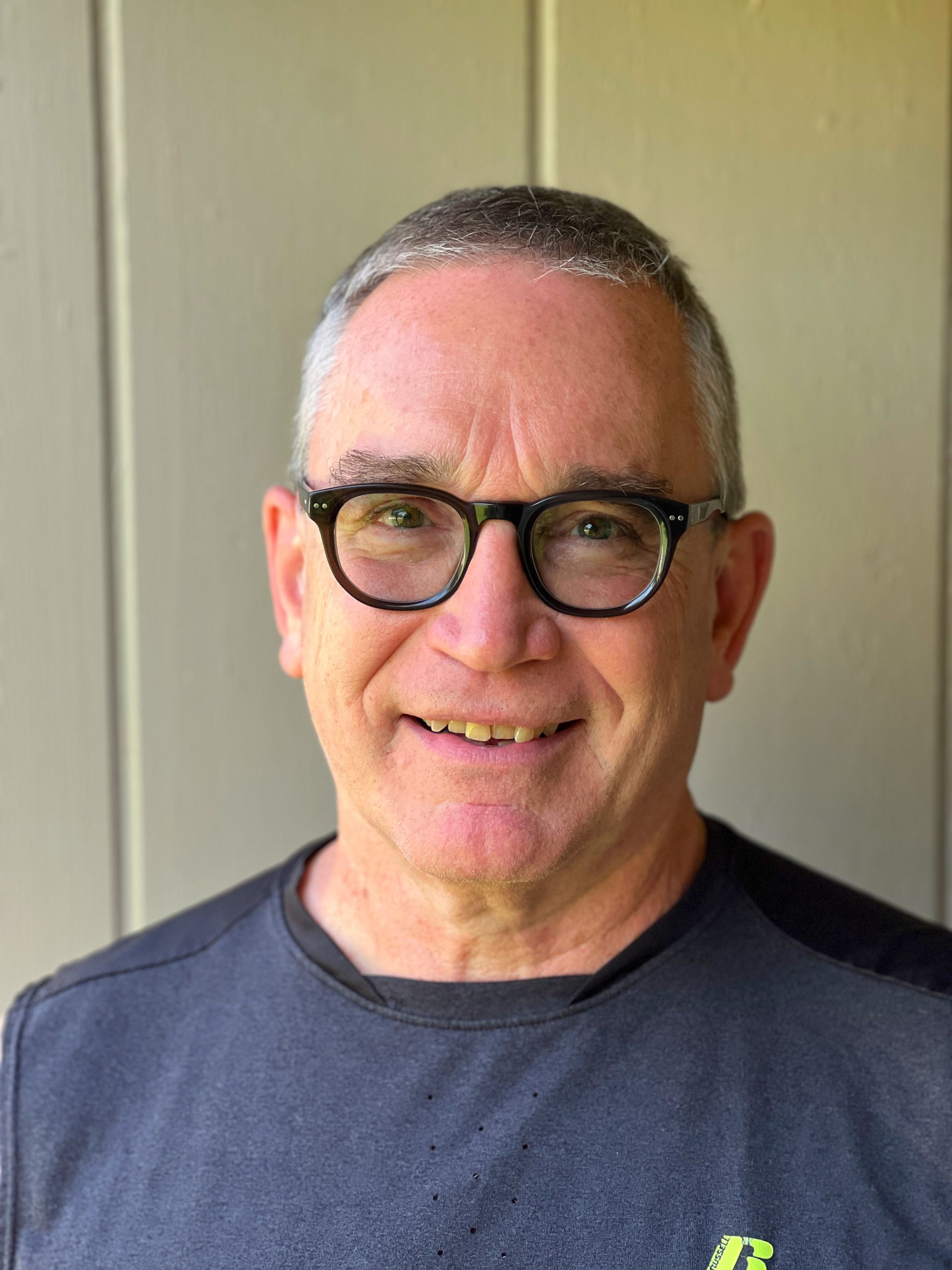 A man wearing glasses and a gray shirt is smiling for the camera.