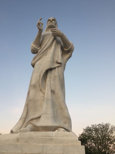 A statue of a man in a white robe stands in front of a blue sky