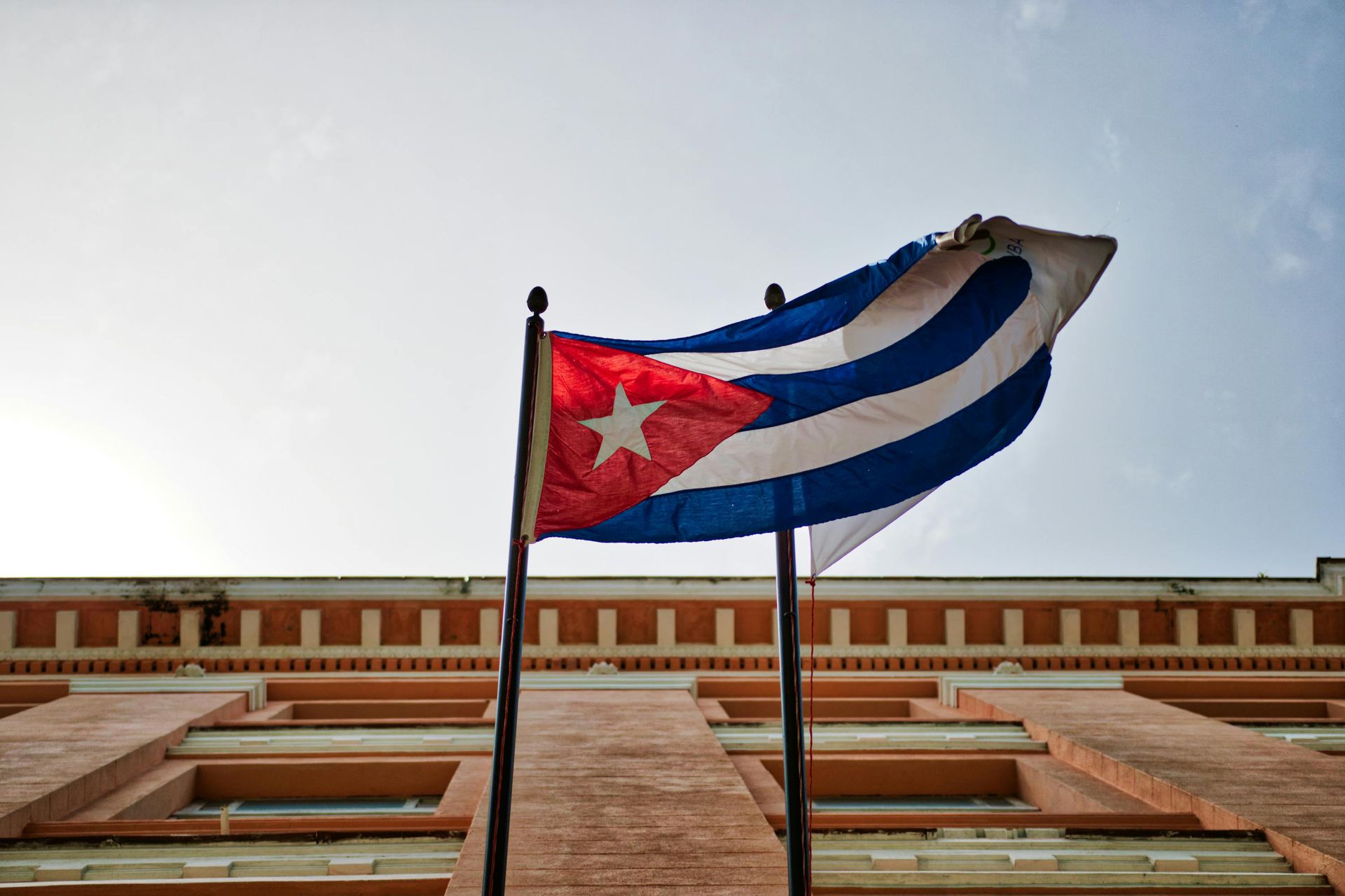 Two cuban flags are waving in front of a building.