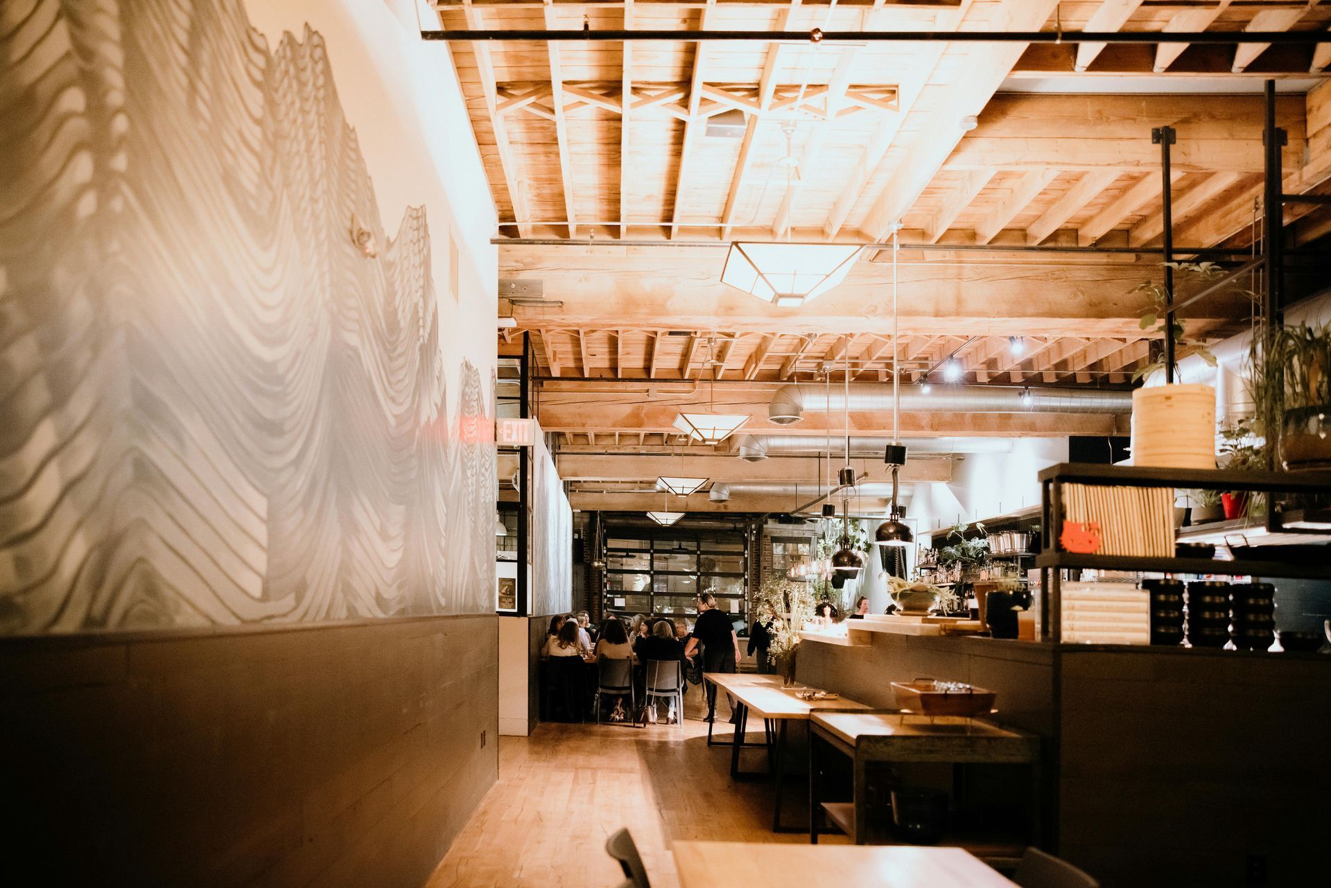 Interior of a restaurant with wooden tables and ceiling, mural on the wall, and people in the background.