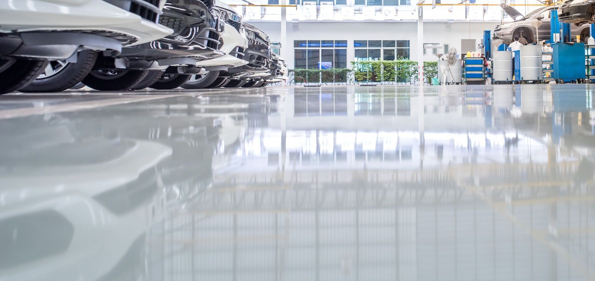 Rangée de véhicules sur un sol brillant et réfléchissant à l'intérieur d'un bâtiment industriel très éclairé.