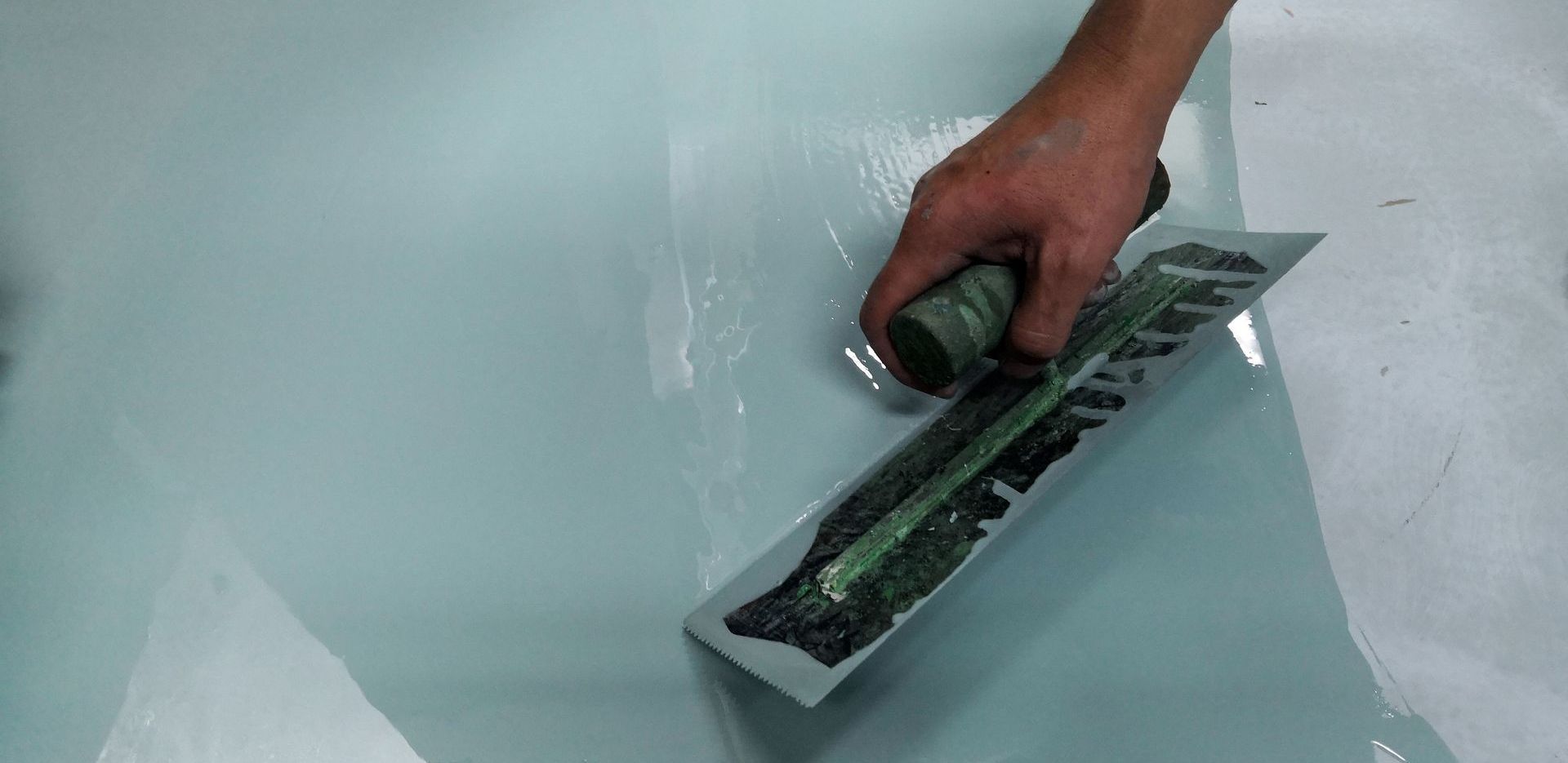 Une main utilisant une truelle pour lisser l'époxy sur une surface bleu clair.