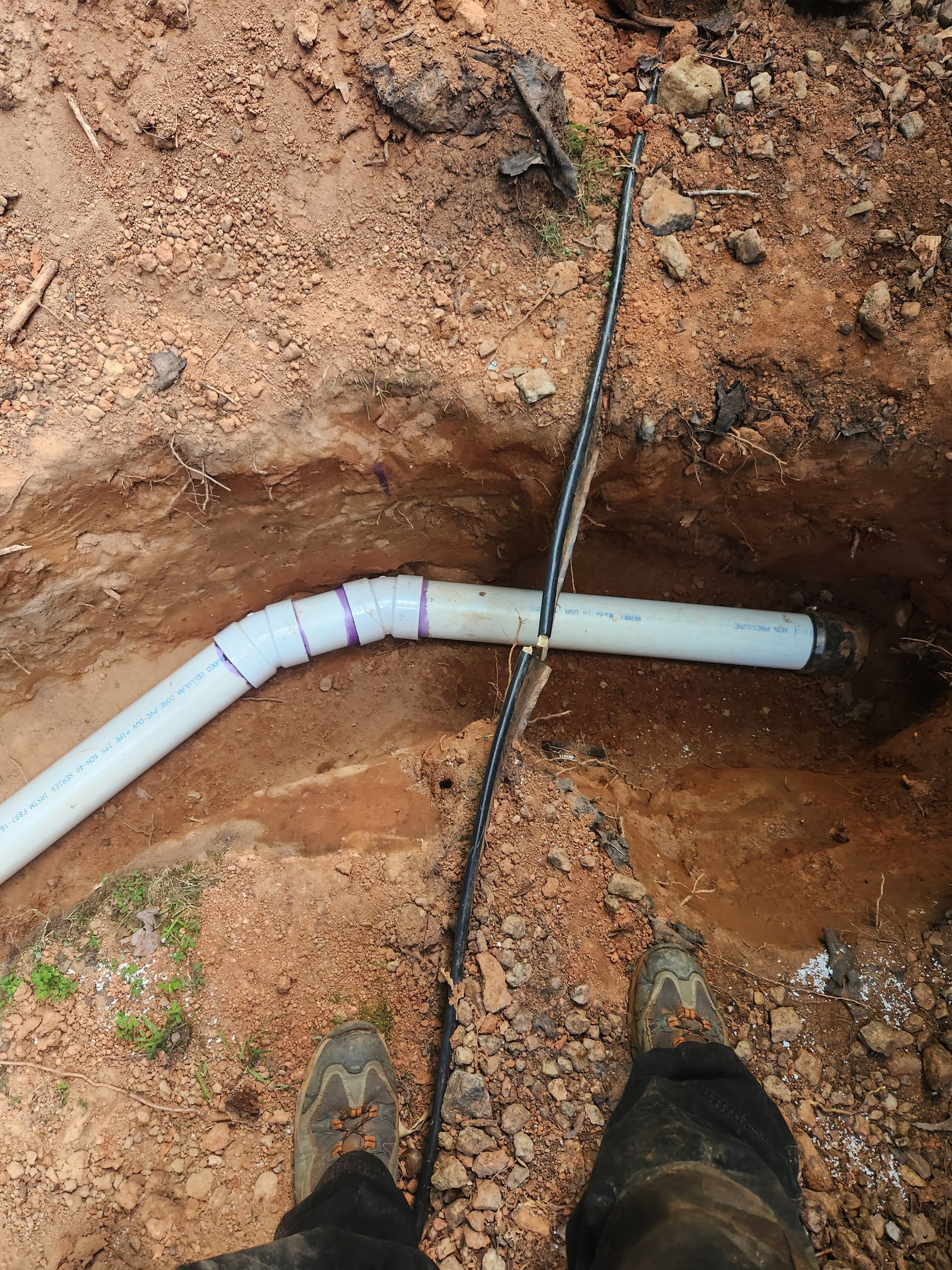 A person is standing next to a pipe in the dirt.