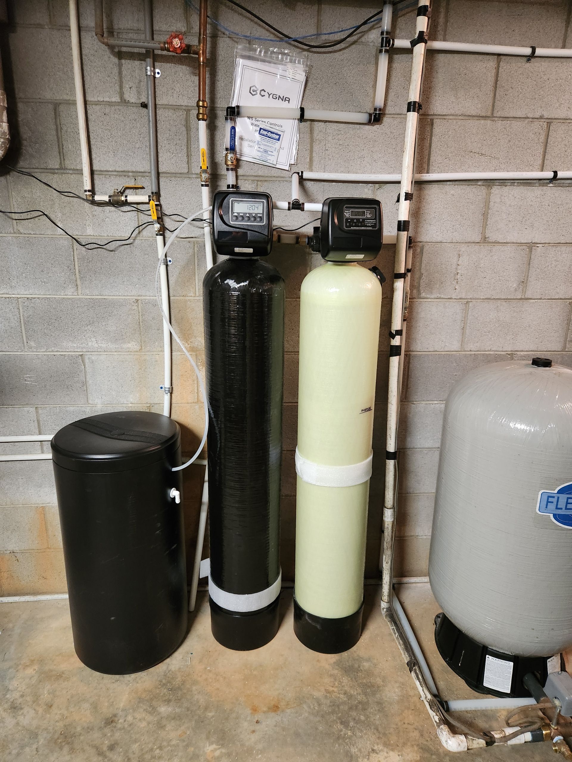 Three water filters are sitting next to each other in a basement.