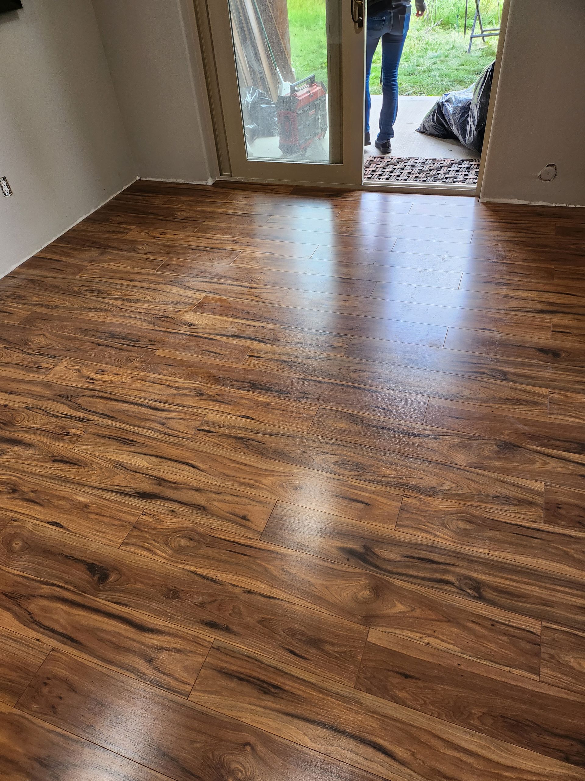A person is standing in a room with a wooden floor and a sliding glass door.