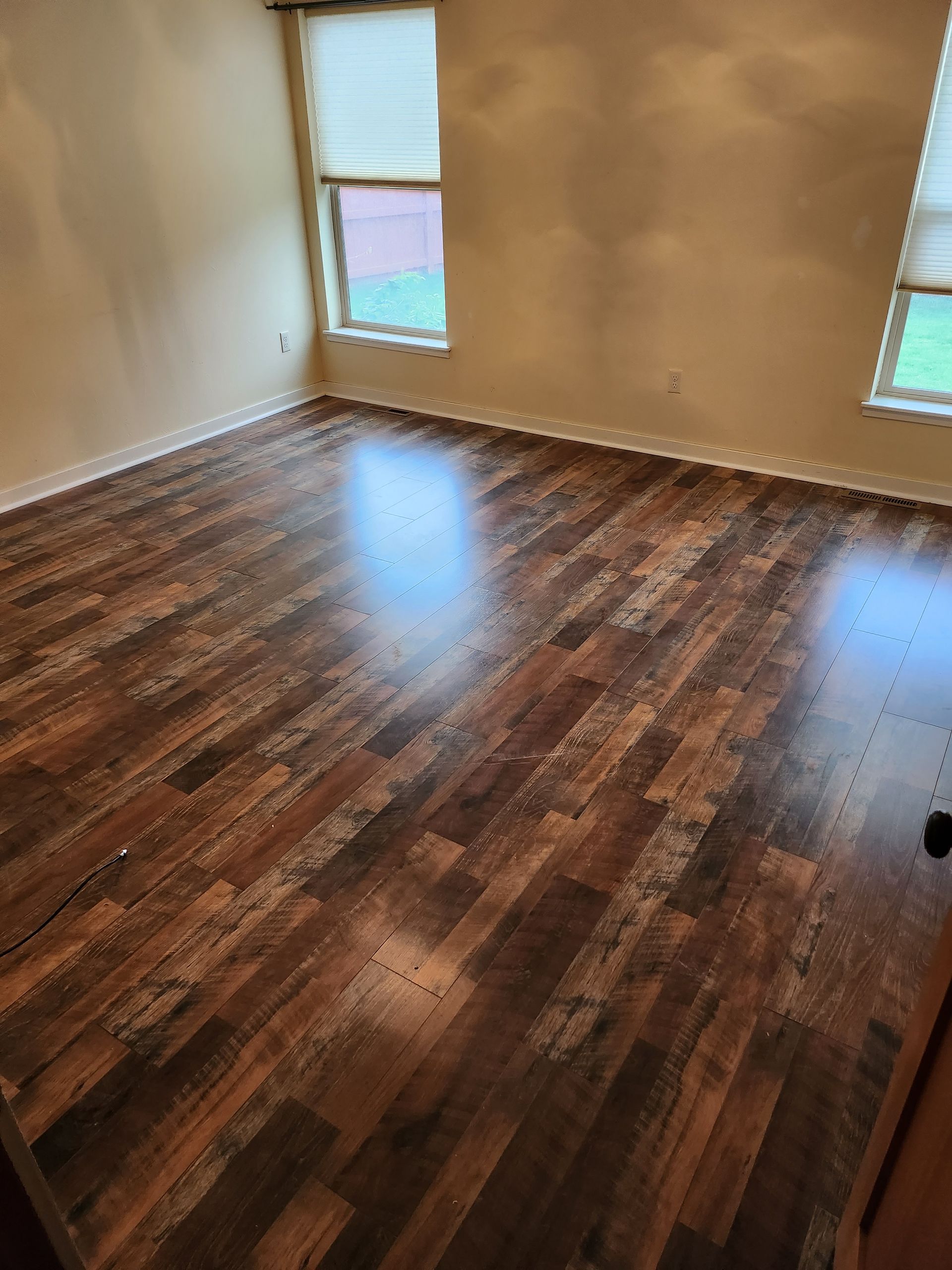 A bedroom with hardwood floors and two windows.