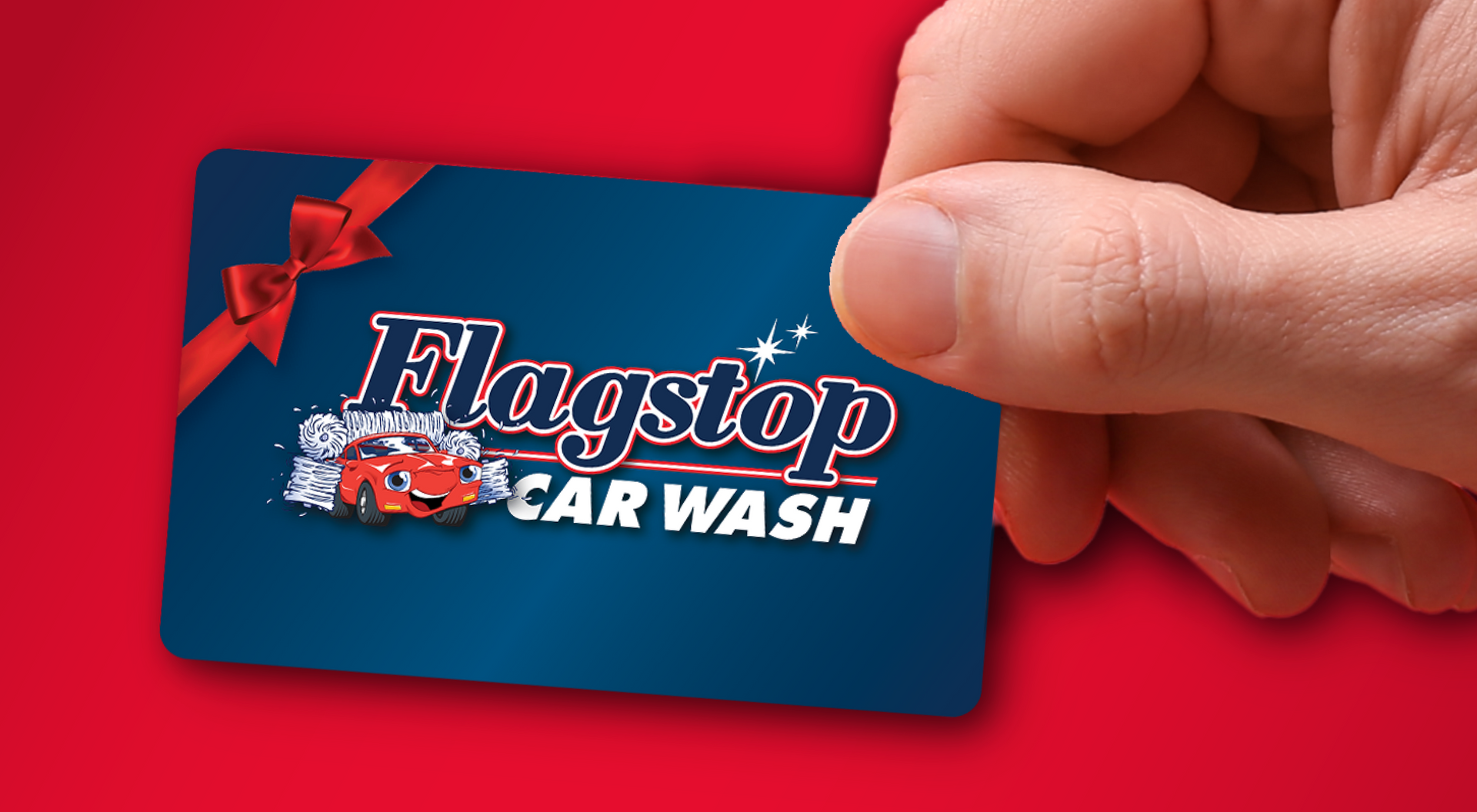 Hand holding a Flagstop Car Wash gift card with a red bow on a red background.