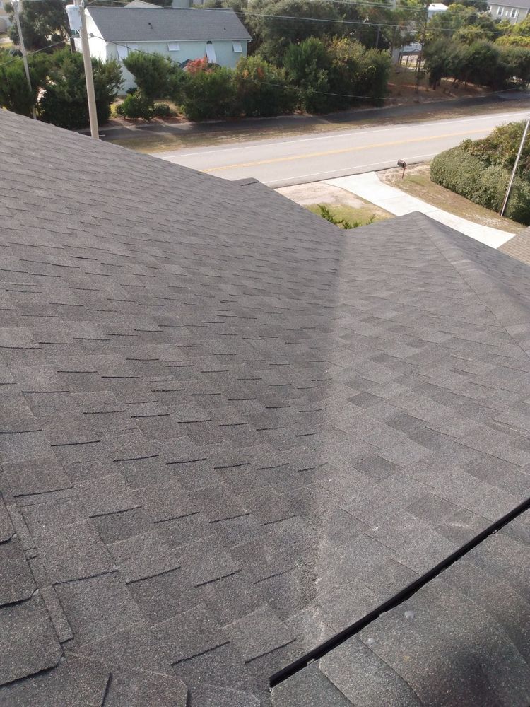 A roof with a lot of shingles on it and a house in the background.