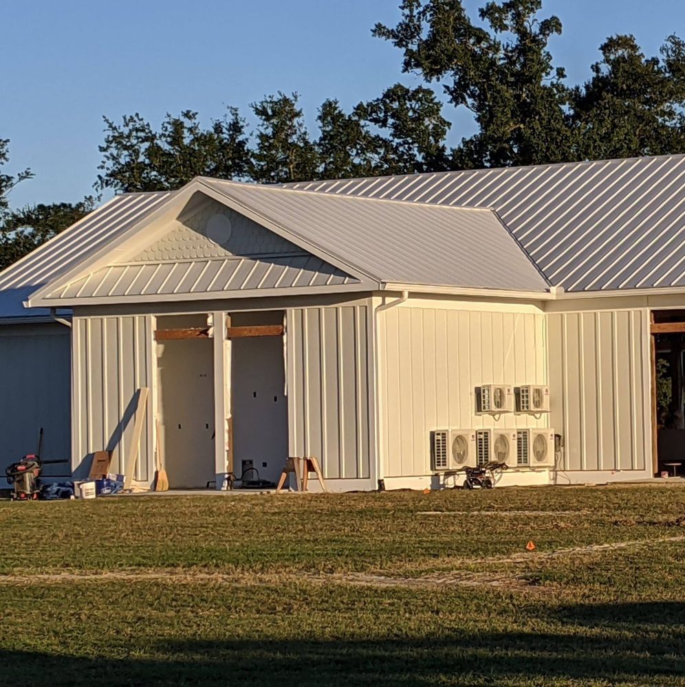 A white building with a metal roof sits in the middle of a grassy field
