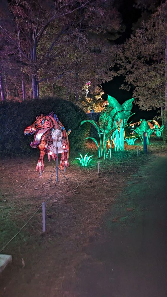 A statue of a dinosaur is lit up at night in a park.