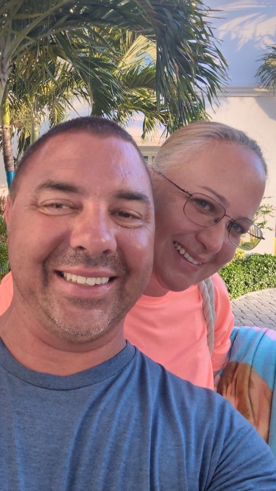 A man and a woman are posing for a selfie in front of a palm tree.