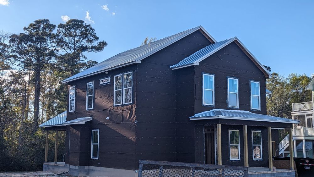 A large brown house with a metal roof is under construction.