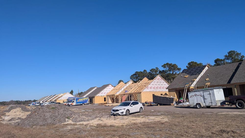 A row of houses under construction with cars parked in front of them.