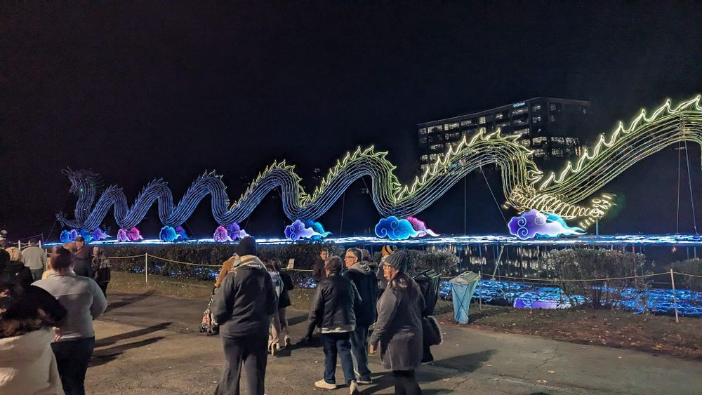 A group of people are standing in front of a large dragon statue at night.