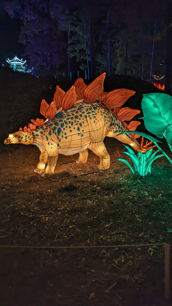 A stegosaurus is walking through a forest at night.