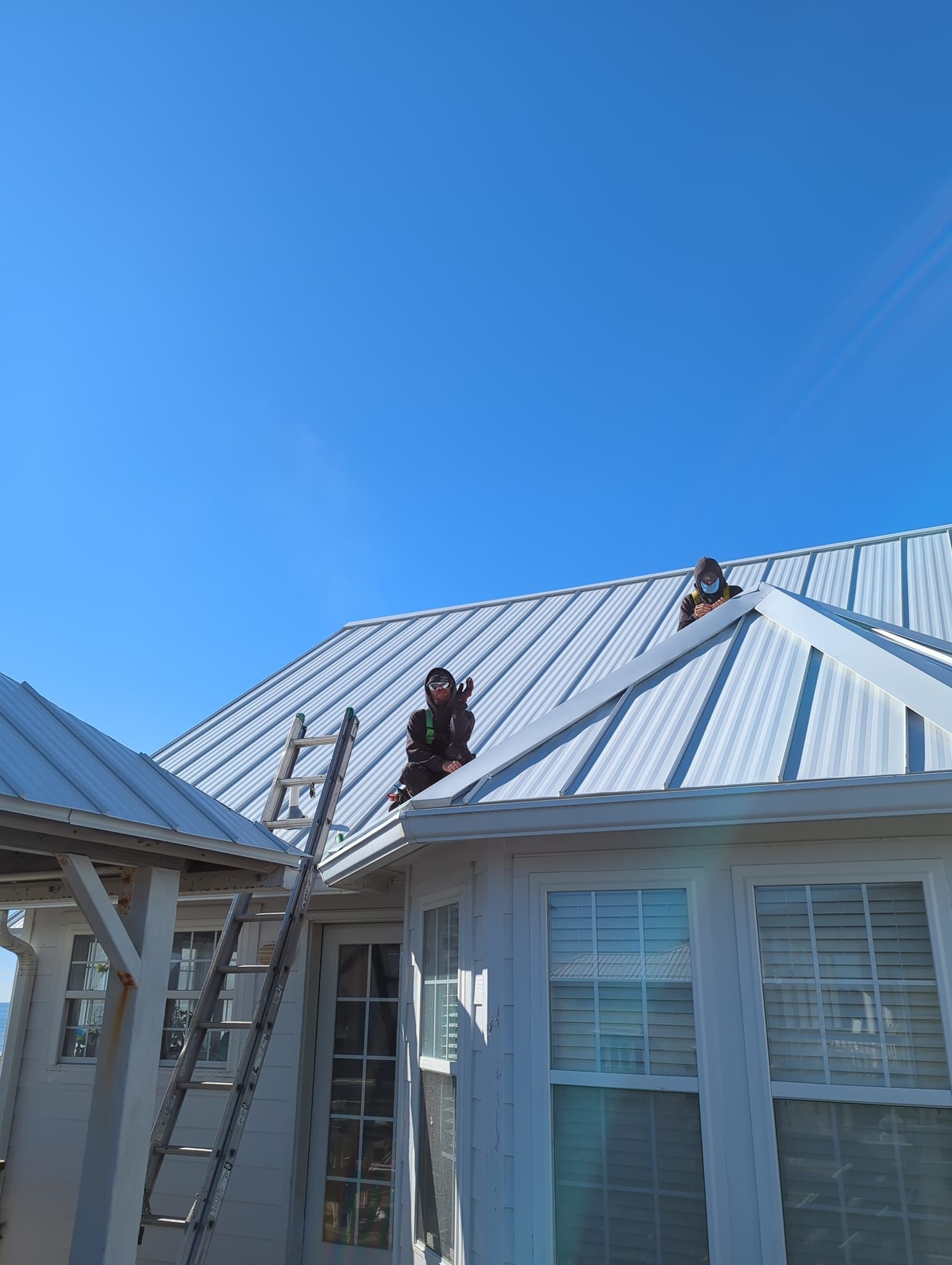 A man is standing on the roof of a house with a ladder.