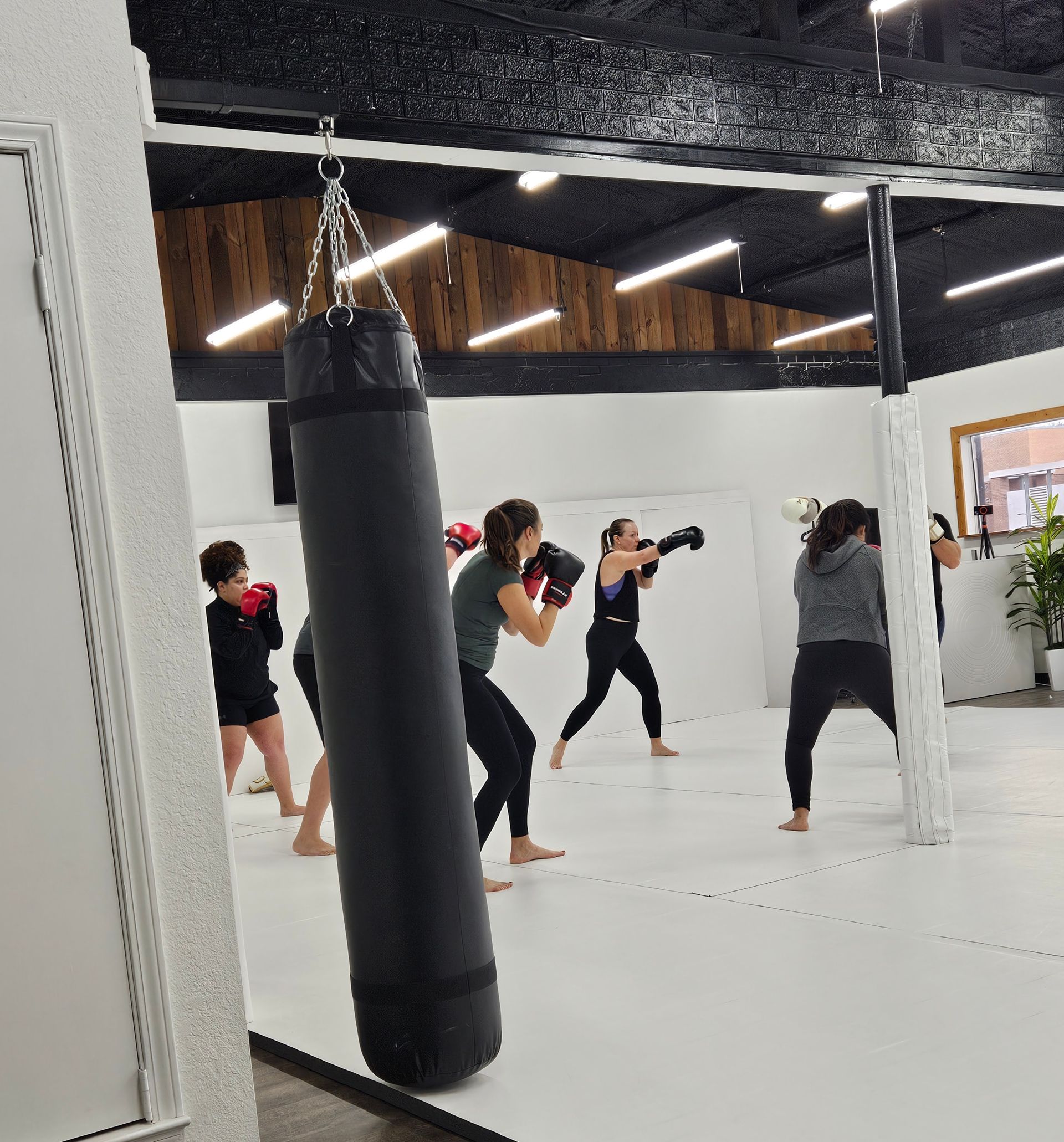 People practicing kickboxing moves at Samurai Brazilian Jiu-Jitsu gym, with a hanging punching bag in the foreground.