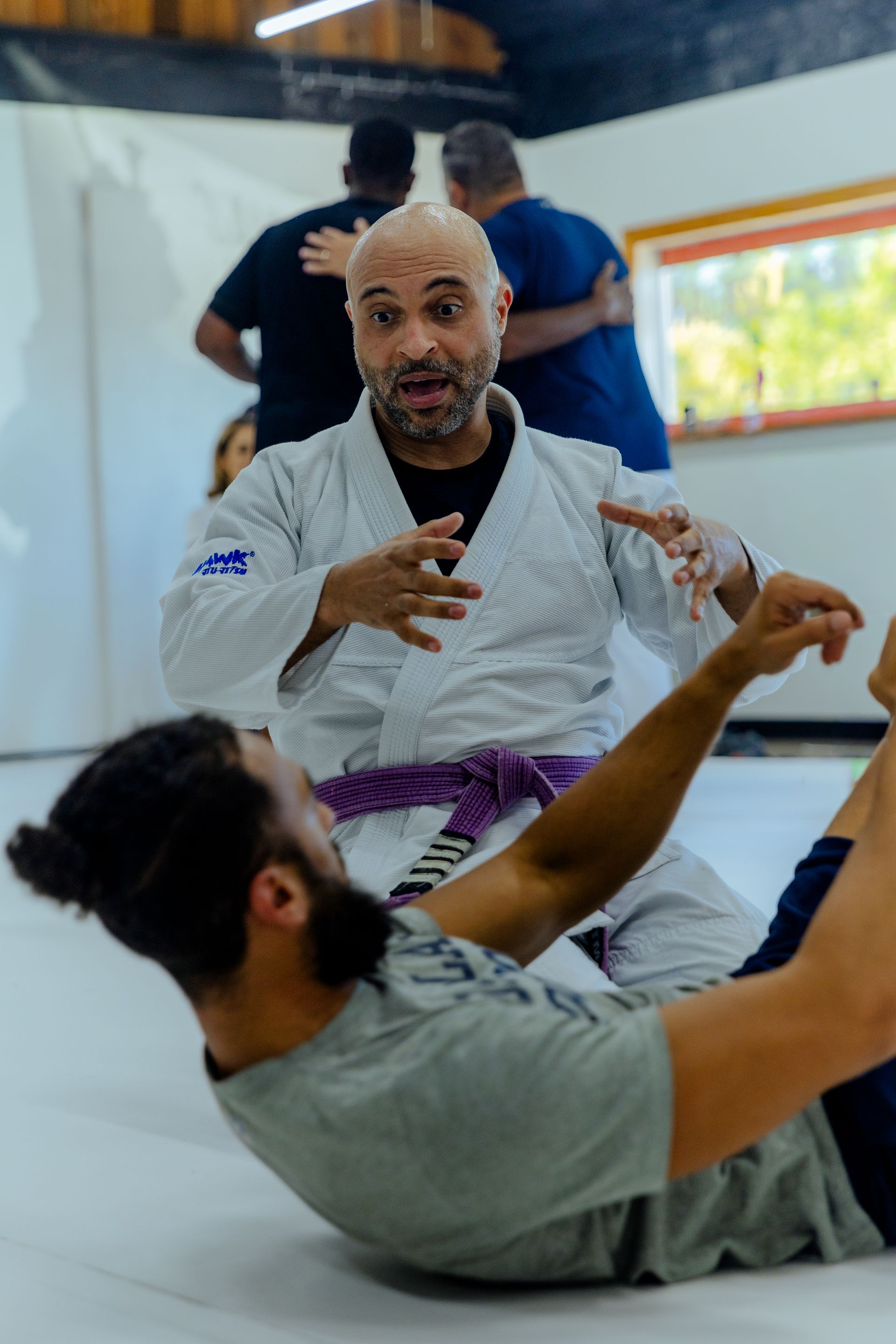 A martial arts instructor with a purple belt demonstrates a technique to a student on a mat at Samurai Brazilian Jiu-Jitsu.