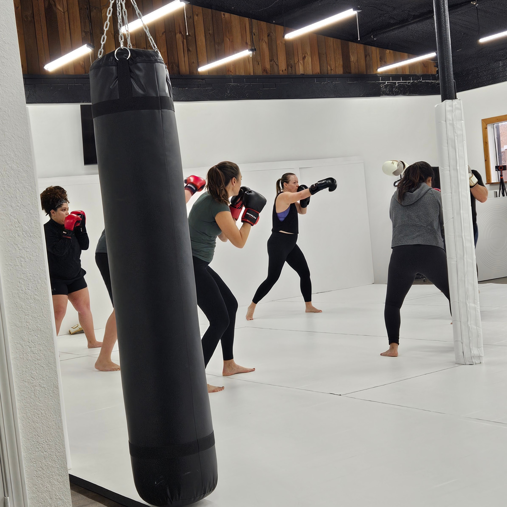 People wearing boxing gloves train at the Samurai Brazilian Jiu-Jitsu gym, practicing punches in a group kickboxing class.